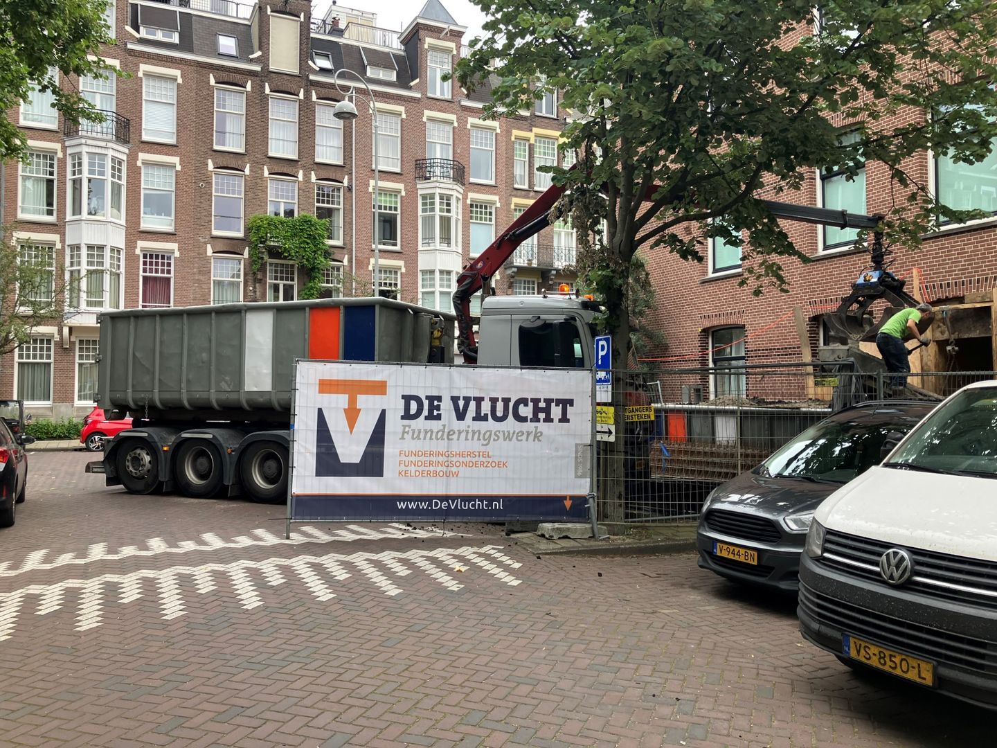 Bouwplaats van De Vlucht in een Amsterdamse straat, met bouwhek, spandoek en kraanwagen