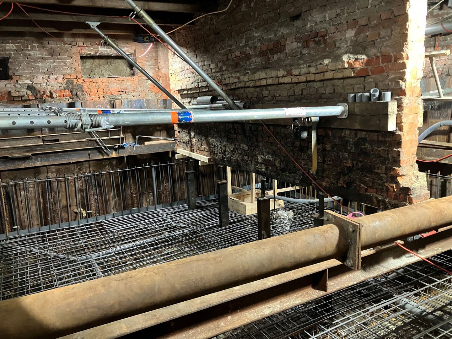 Oude bakstenen muur, ondersteund door stalen stempels, boven nieuw wapeningsstaal voor de fundering
